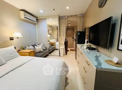 Modern bedroom with cozy seating area and large TV, perfect for relaxation.