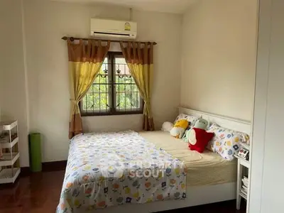 Cozy bedroom with colorful bedding and window view, featuring air conditioning and wooden flooring.