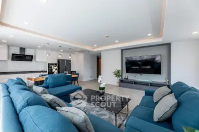 Spacious modern living room with blue sofas and large TV, open kitchen layout, perfect for entertaining.
