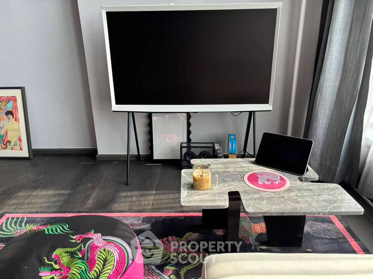 Modern living room with stylish decor and large flat-screen TV, vibrant rug, and sleek furniture.