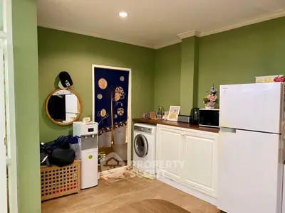 Charming kitchen with green walls, featuring a washing machine and fridge, perfect for modern living.