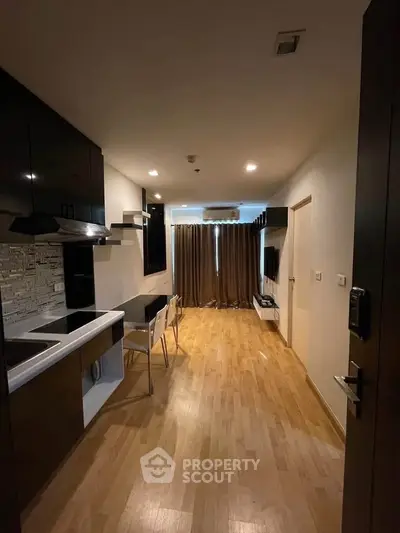 Modern apartment interior with sleek kitchen and cozy living area, featuring wooden flooring and stylish furnishings.