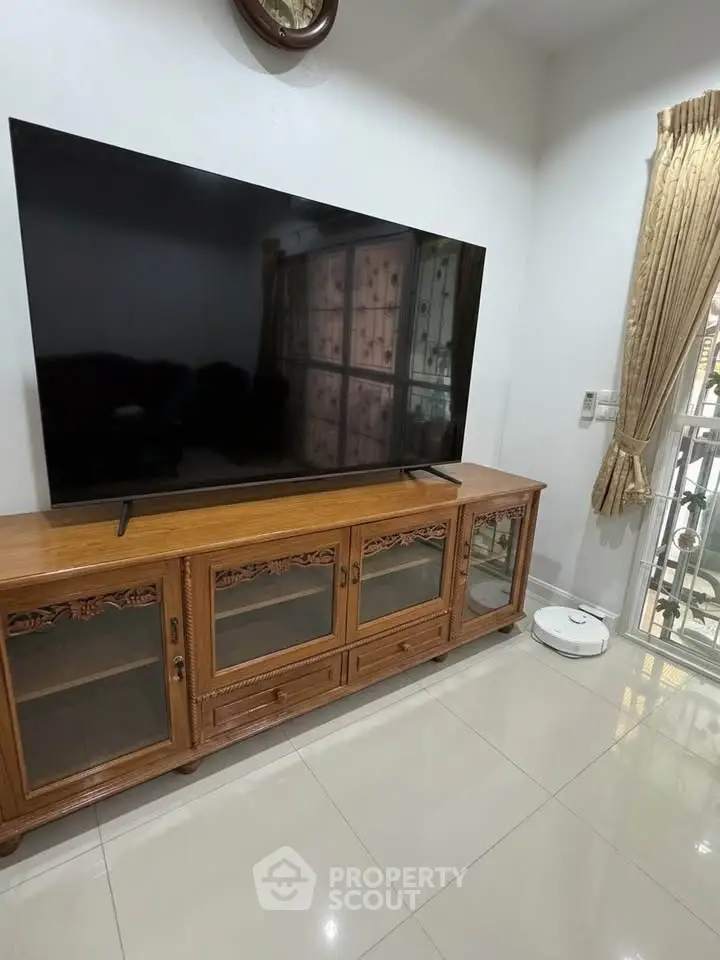 Spacious living room with elegant wooden TV stand and large flat-screen TV, featuring modern decor and natural light.
