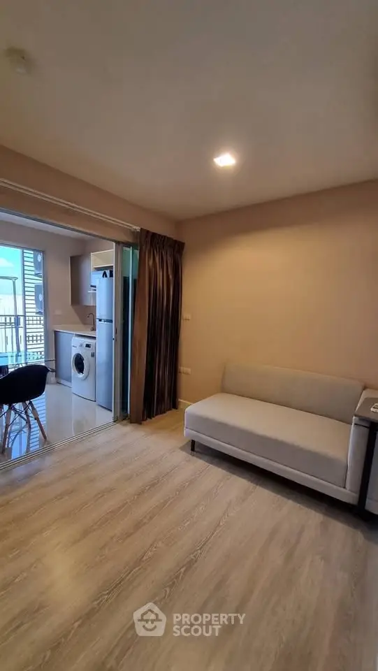 Modern living room with open kitchen and washing machine, featuring a cozy sofa and balcony view.
