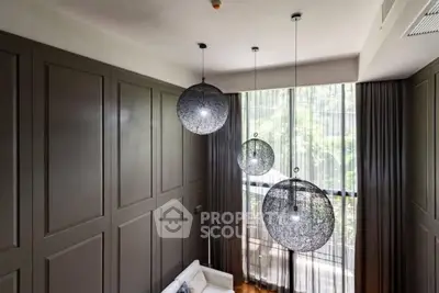 Elegant living room with high ceilings and modern pendant lights, featuring large windows with lush garden views.