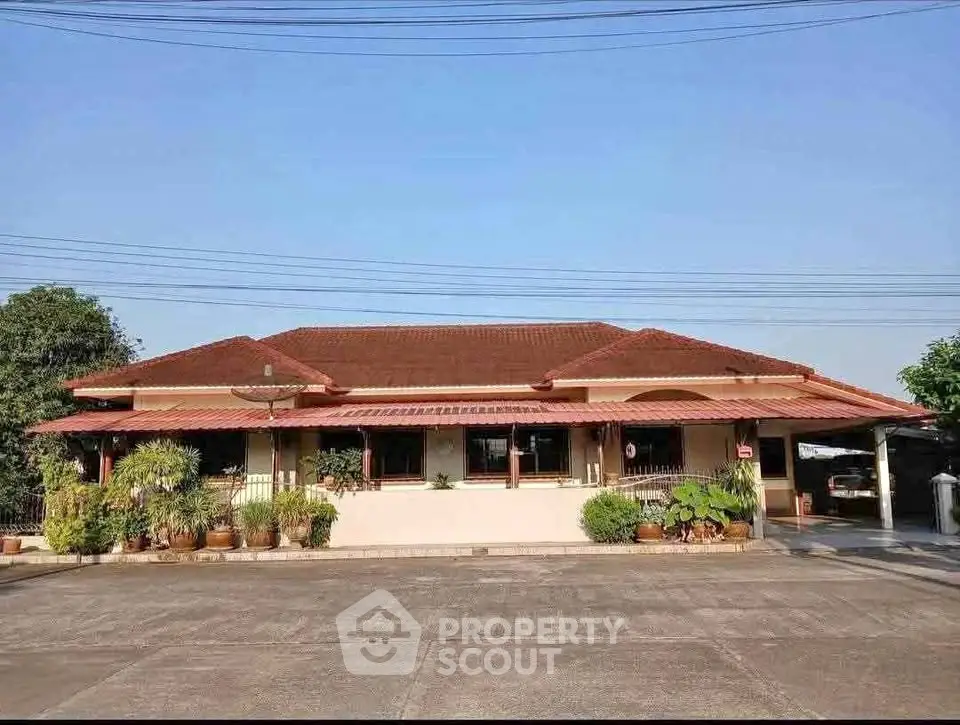 Charming single-story home with red roof and spacious driveway, surrounded by lush greenery.