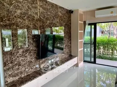 Luxurious living room with marble accent wall and large TV, overlooking a lush garden view.