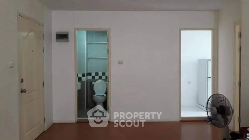 Minimalist apartment interior with bathroom and kitchen access, featuring a fan and simple decor.