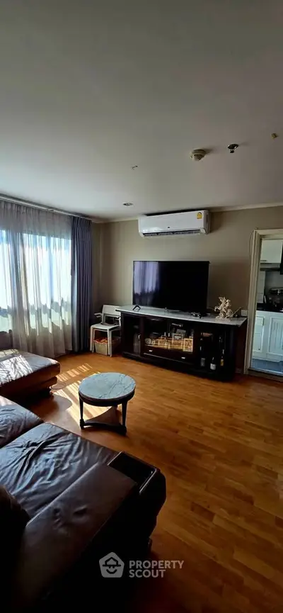 Spacious living room with hardwood floors, large TV, and natural light from windows.