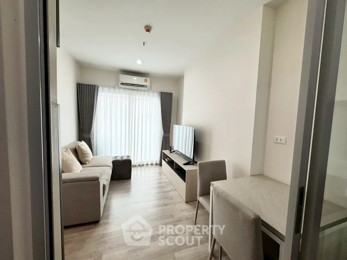 Modern living room with cozy sofa, flat-screen TV, and natural light from large window.