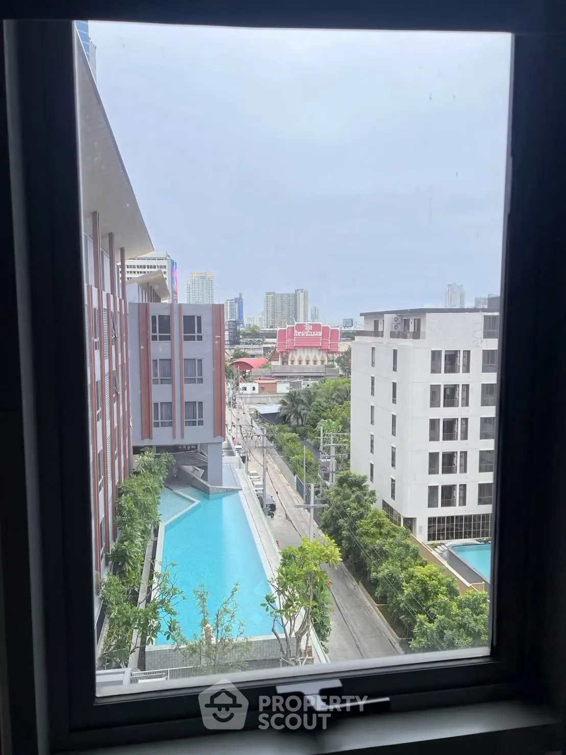 Stunning cityscape view from a high-rise window overlooking modern buildings and a sleek swimming pool.