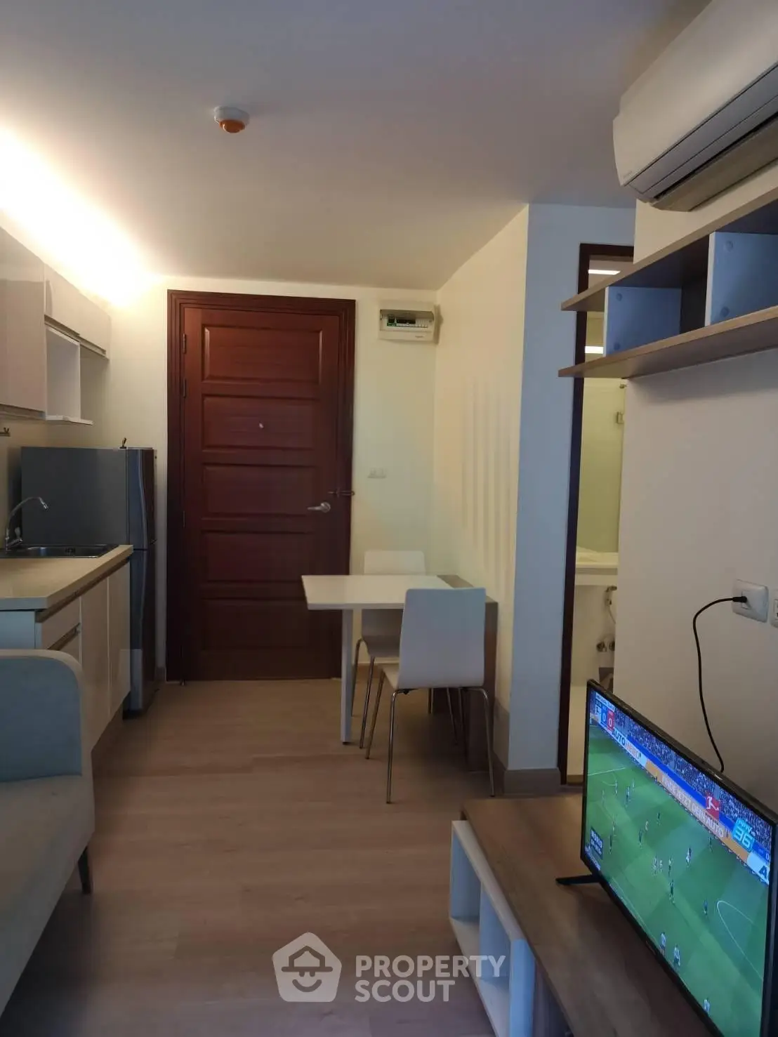 Modern compact living room with open kitchen and cozy dining area, featuring air conditioning and TV setup.
