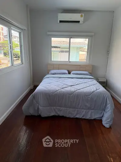 Cozy bedroom with wooden floors and large windows, featuring a comfortable double bed and air conditioning.