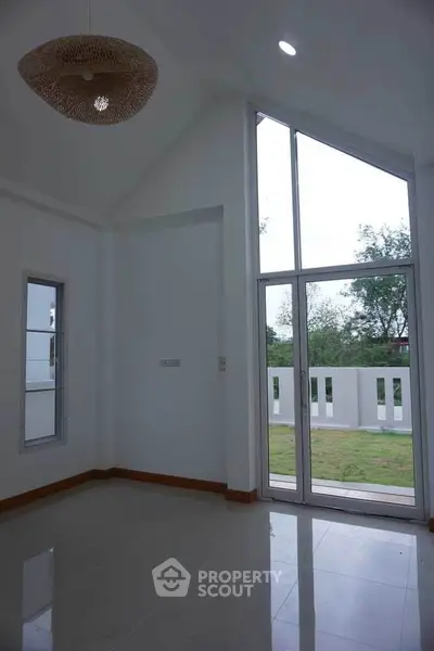 Spacious room with high ceilings and large windows overlooking a garden.