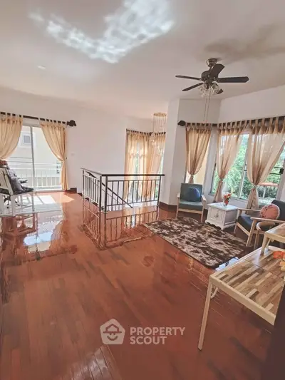 Spacious living room with polished wooden floors, elegant curtains, and ceiling fan, offering a cozy and bright ambiance.