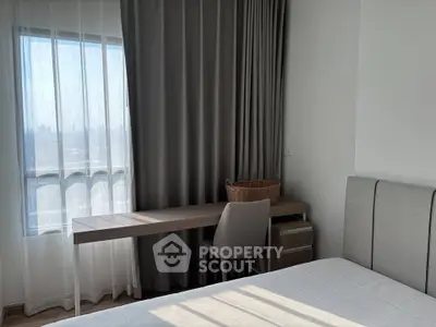 Modern bedroom with natural light, featuring a sleek desk and comfortable chair by the window.