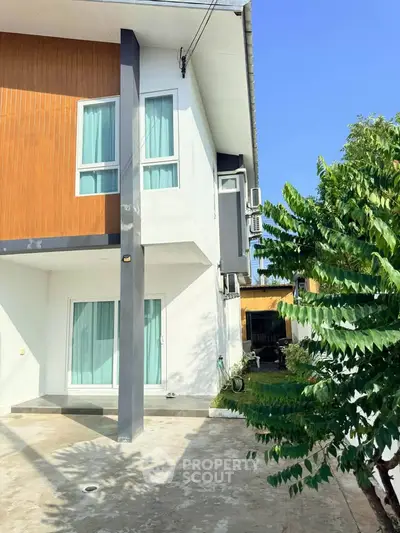 Modern two-story house with large windows and sleek design, featuring a spacious driveway and lush greenery.