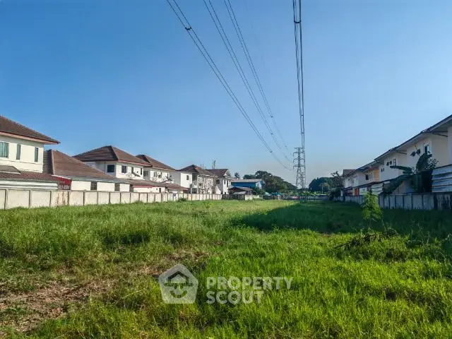 Expansive green field in a residential area with potential for development, under clear blue skies, surrounded by suburban homes.
