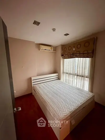 Cozy bedroom with air conditioning and natural light, featuring a comfortable bed and wooden flooring.