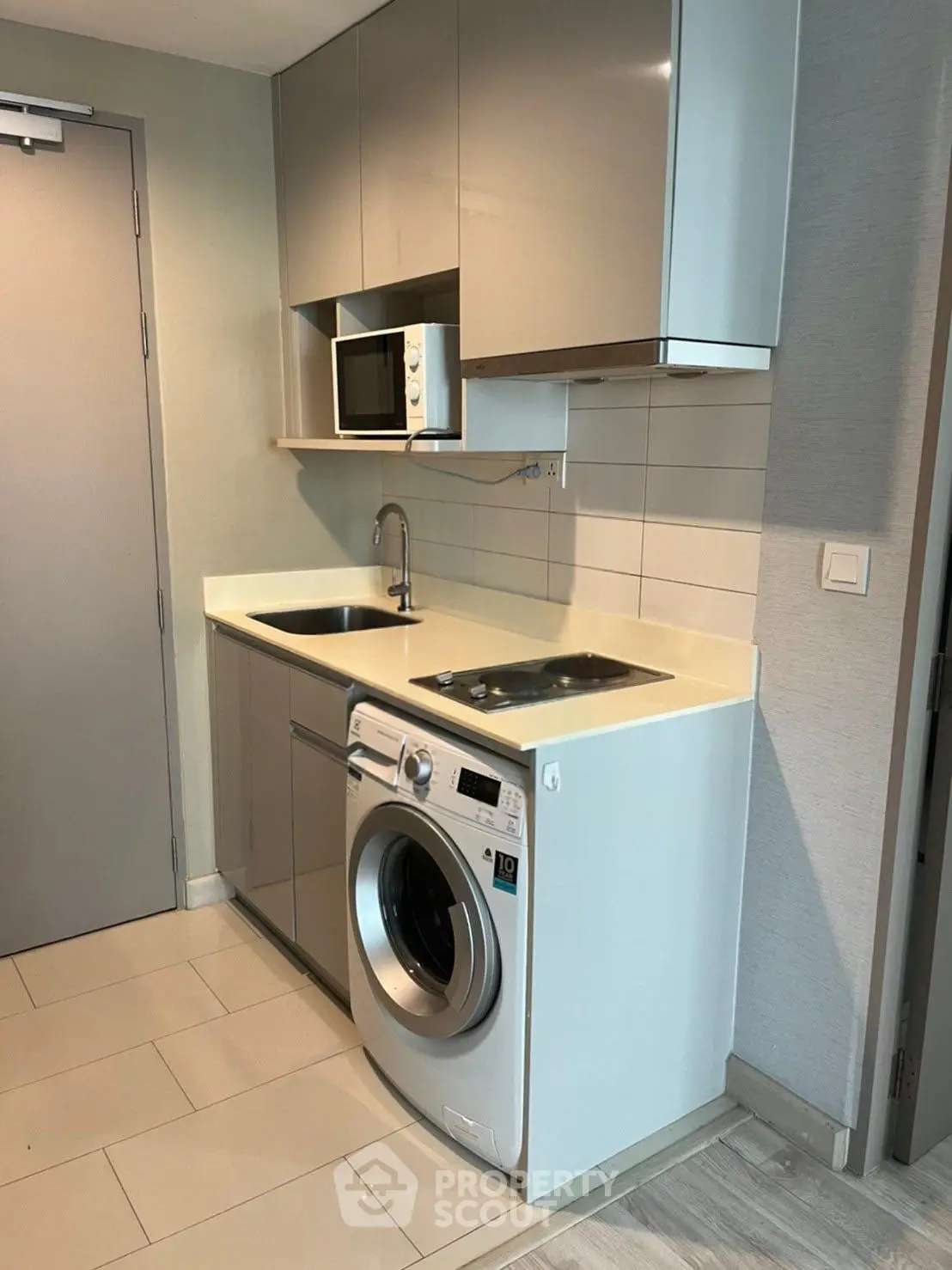 Compact modern kitchen with washing machine and microwave in sleek apartment.