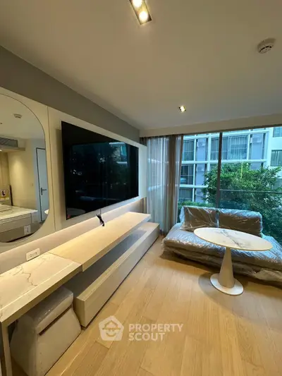 Modern living room with large TV and floor-to-ceiling windows offering garden views.