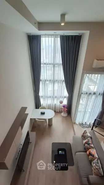 Modern living room with high ceilings and large windows, featuring stylish decor and natural light.