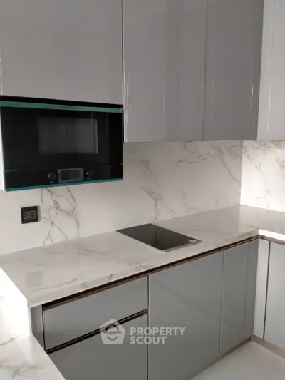 Modern kitchen with sleek cabinetry and marble countertops, featuring a built-in oven and electric cooktop.