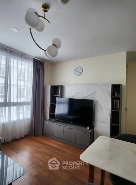 Modern living room with stylish decor and large TV, featuring elegant lighting and natural light from large windows.