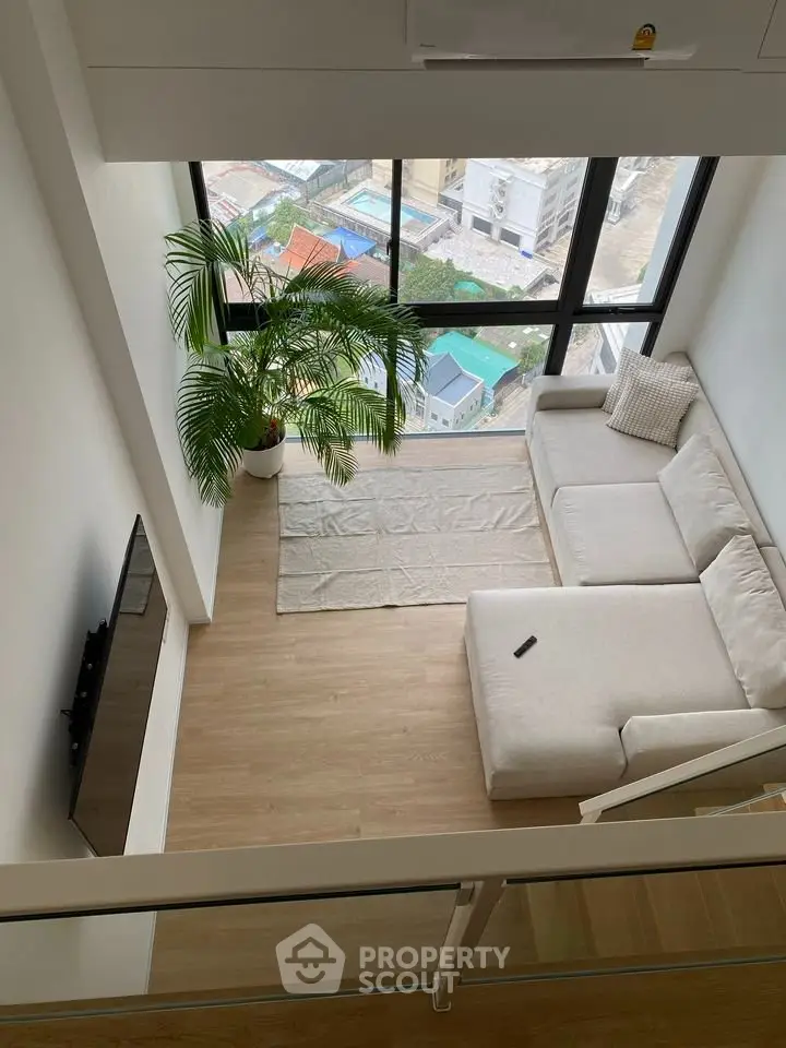 Modern living room with large windows and city view, featuring a cozy L-shaped sofa and a flat-screen TV.