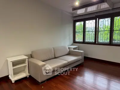 Spacious living room with elegant sofa and large windows offering lush green views.