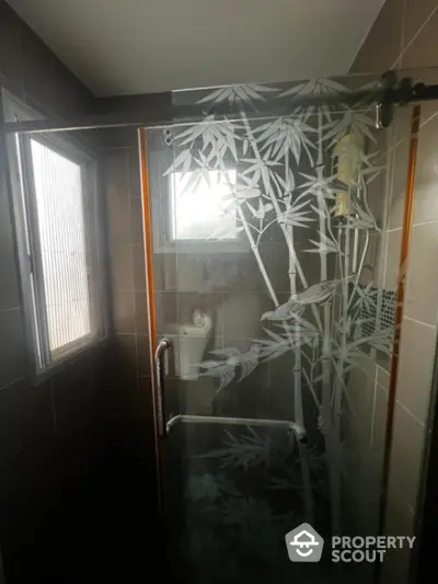 Elegant bathroom with artistically etched glass shower enclosure and natural light filtering through frosted window, enhancing the serene ambiance.