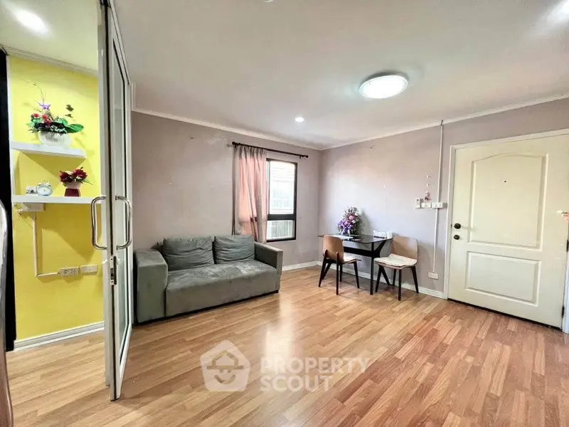 Cozy living room with wooden flooring, sofa, and dining area in modern apartment.