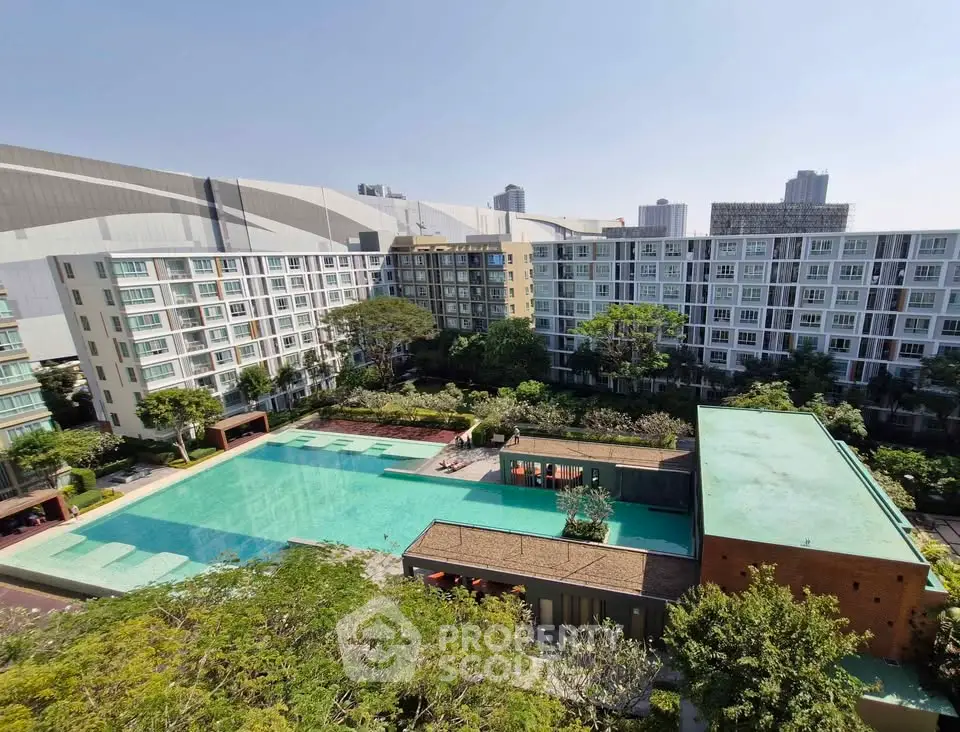 Stunning aerial view of modern apartment complex with large swimming pool and lush greenery.