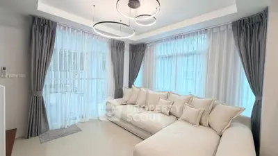 Elegant living room with modern chandelier and plush sectional sofa, featuring large windows with sheer curtains.