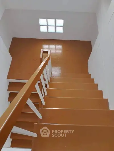 Modern staircase with wooden steps and white railing in a bright interior space.