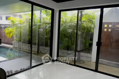 Modern living room with large glass doors opening to a lush garden and pool area, offering serene views.