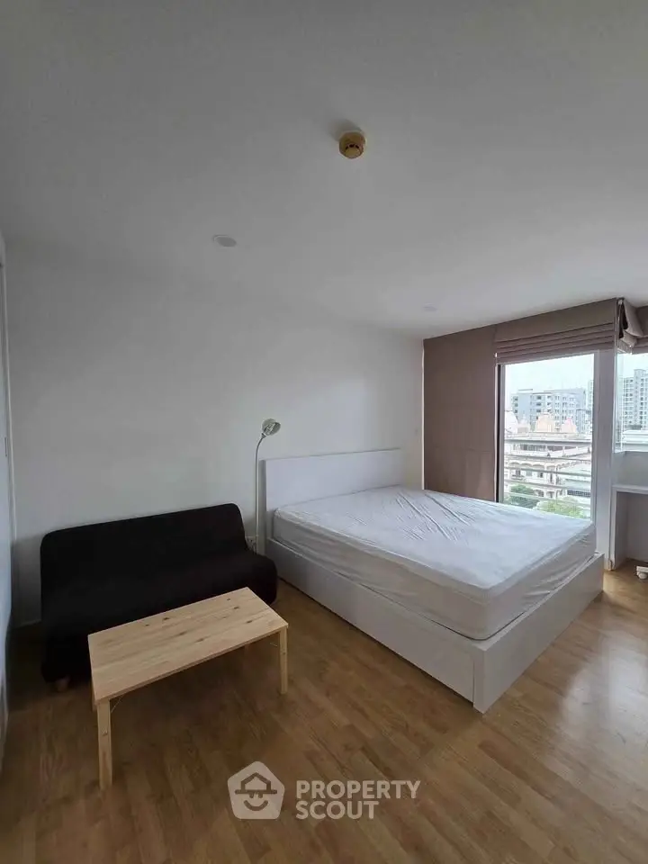 Spacious bedroom with city view, featuring a cozy bed, sofa, and wooden flooring.