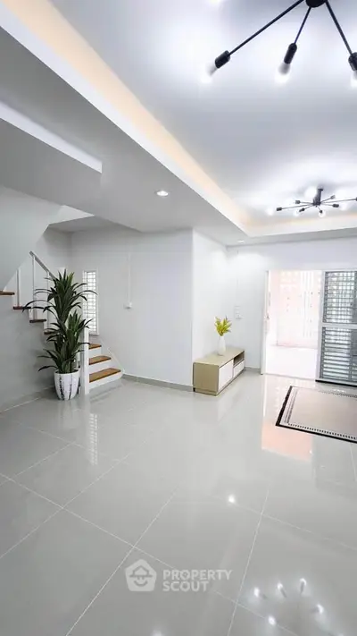 Spacious modern living room with sleek tile flooring and elegant lighting, featuring a staircase and stylish decor.