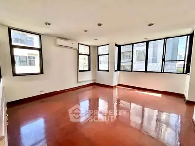 Spacious sunlit room with polished floors and large windows in modern building.