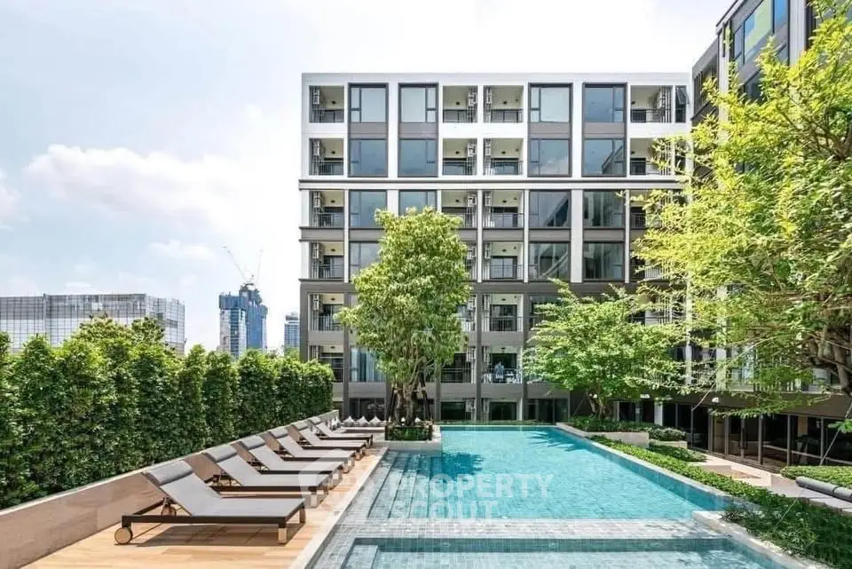 Modern apartment building with pool and sun loungers, lush greenery, and city skyline view.