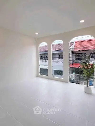 Bright room with large arched windows offering a view of red-roofed houses, perfect for natural light lovers.