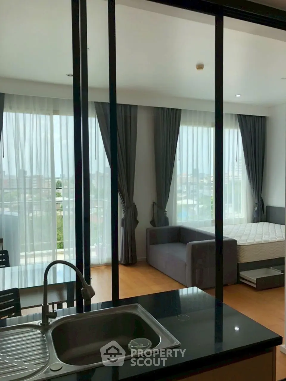 Modern studio apartment with open layout and large windows offering city views.