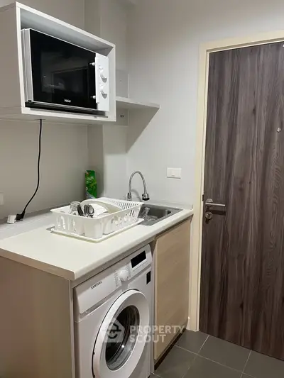 Compact kitchen with washing machine and microwave in modern apartment