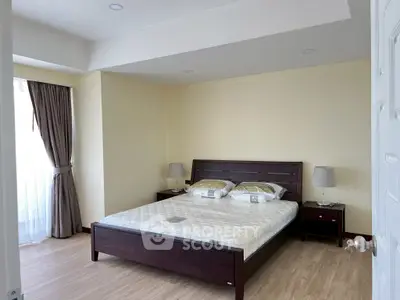 Spacious bedroom with elegant wooden bed and natural light from large window.