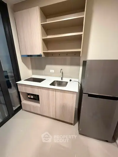 Modern compact kitchen with sleek cabinetry and stainless steel fridge in a stylish apartment.