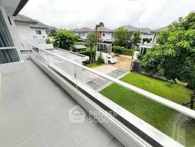 Spacious balcony with glass railing overlooking a lush garden and modern neighborhood.