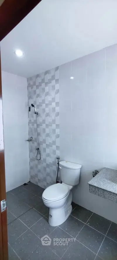 Modern bathroom with sleek design and tiled walls, featuring a toilet and shower area.
