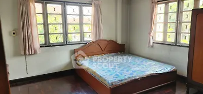 Cozy bedroom with large windows and natural light, featuring a wooden bed frame and parquet flooring.