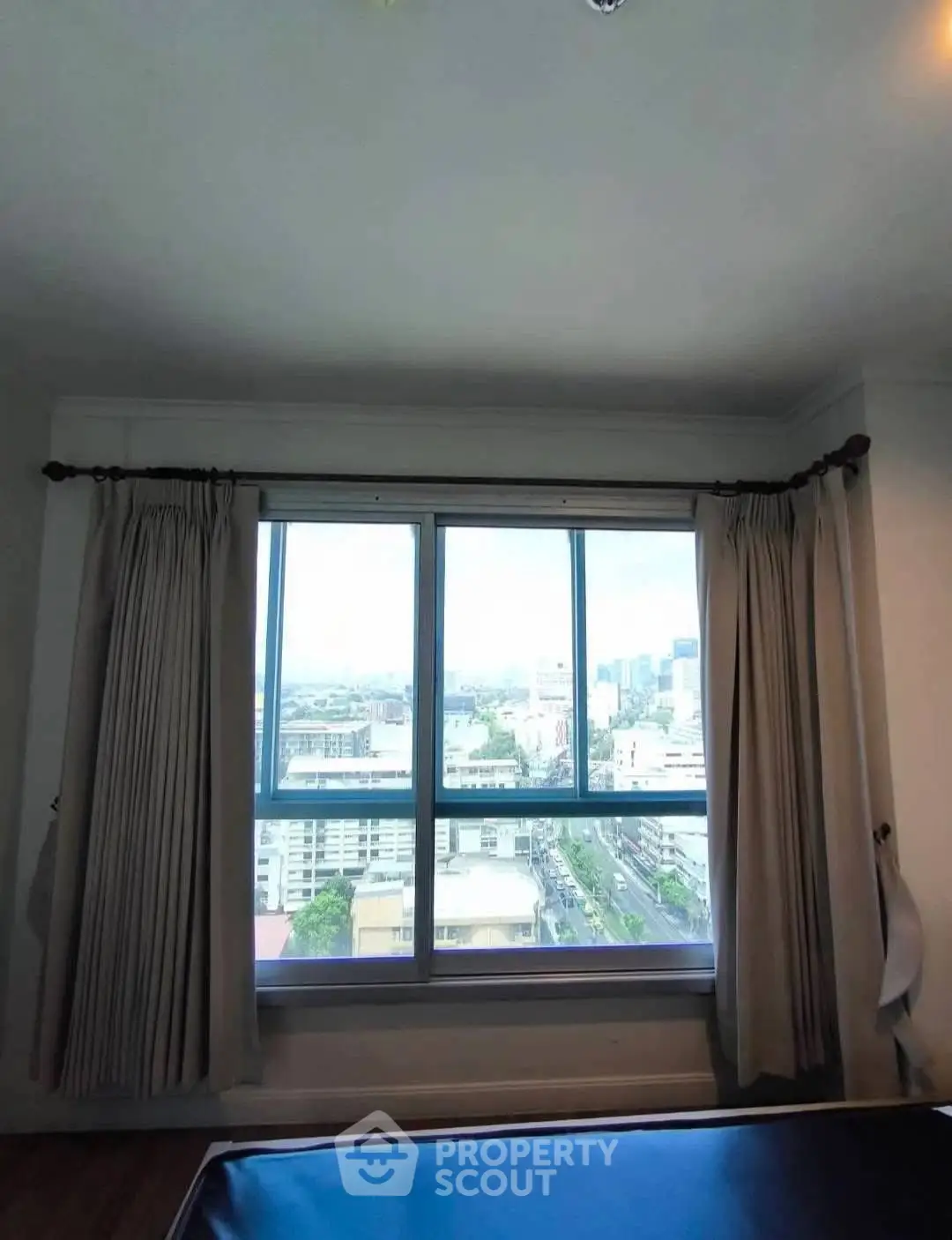 Spacious bedroom with large window offering stunning city views in high-rise apartment.