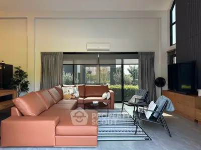 Spacious modern living room with leather sofa and large windows overlooking garden.